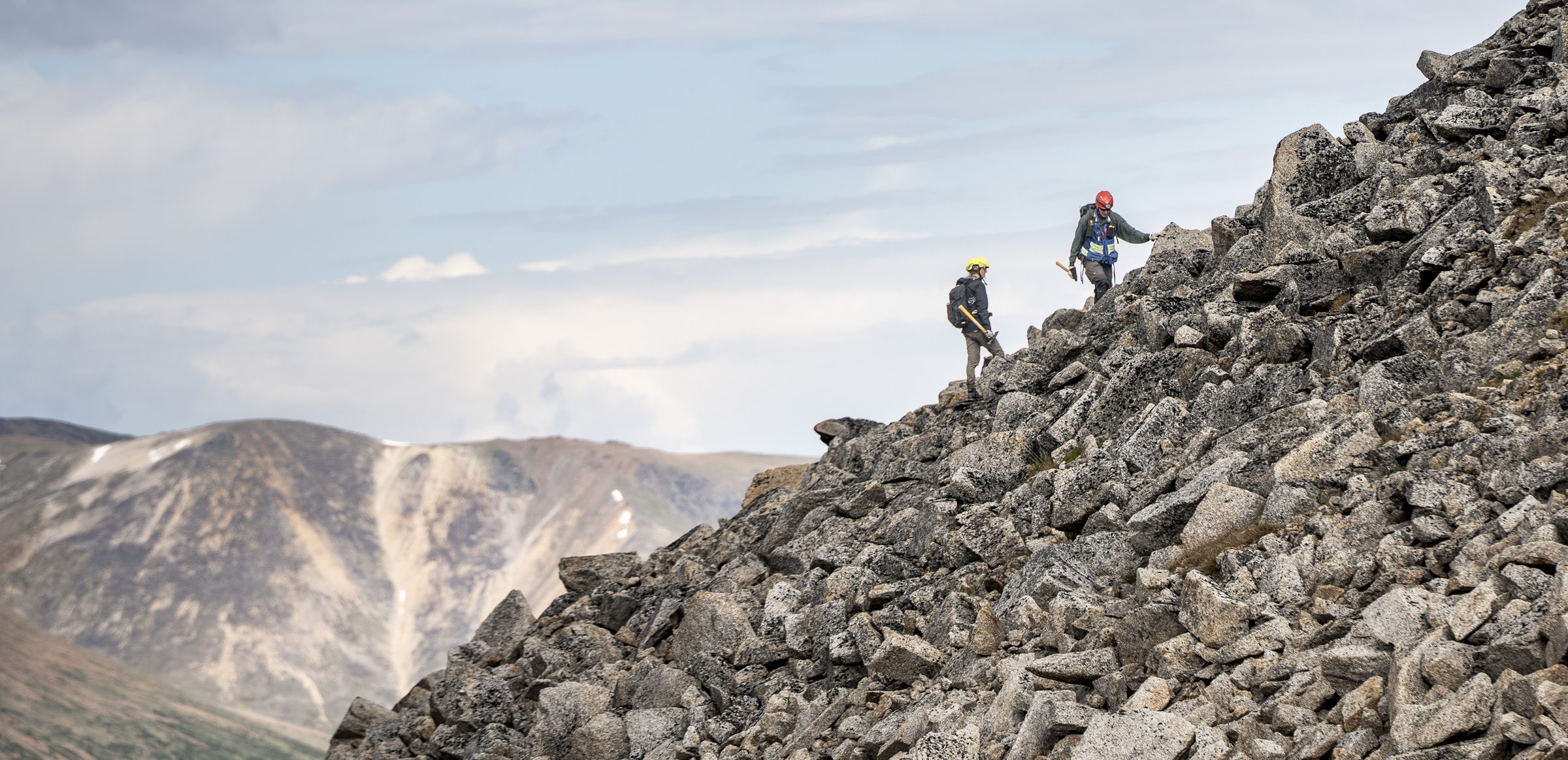 Two geologists with rock hammers traversing a granite scree slope high in the British Columbia mountains